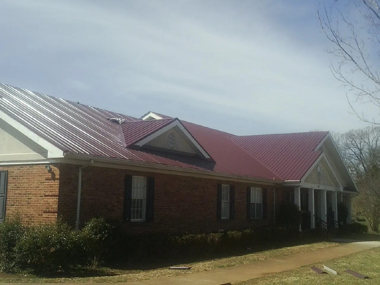 Red metal roof with gabled entries on a long brick building, from a Hail Damage Roof Repair job in Tavernier