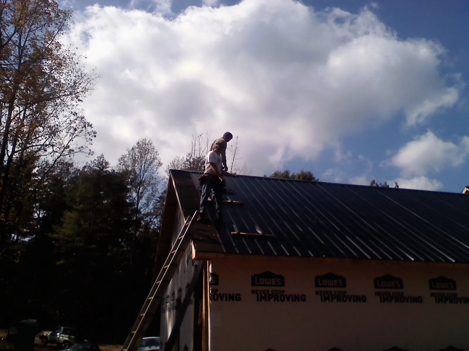 Roofer fastening dark metal panels high against a cloudy sky, from a Roof Inspection job in Tavernier