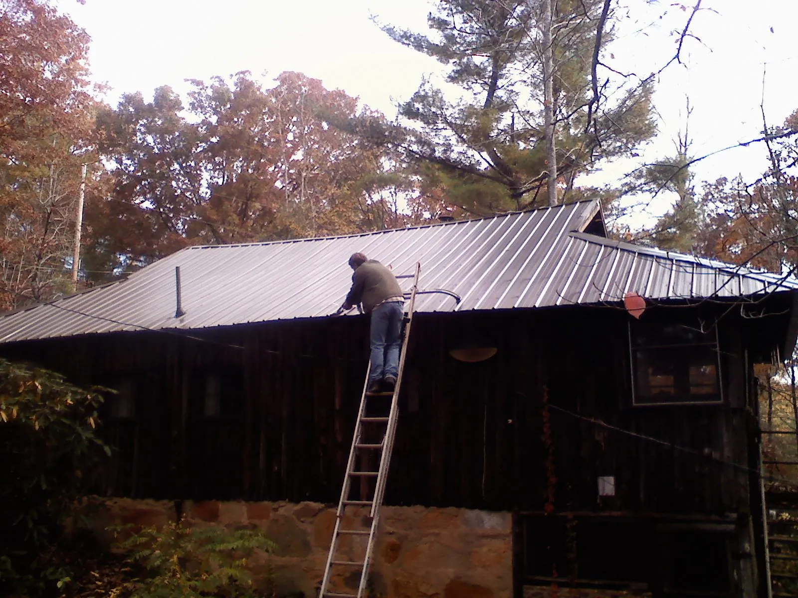 Roofer on a ladder working along the edge of a cabin metal roof in Tavernier