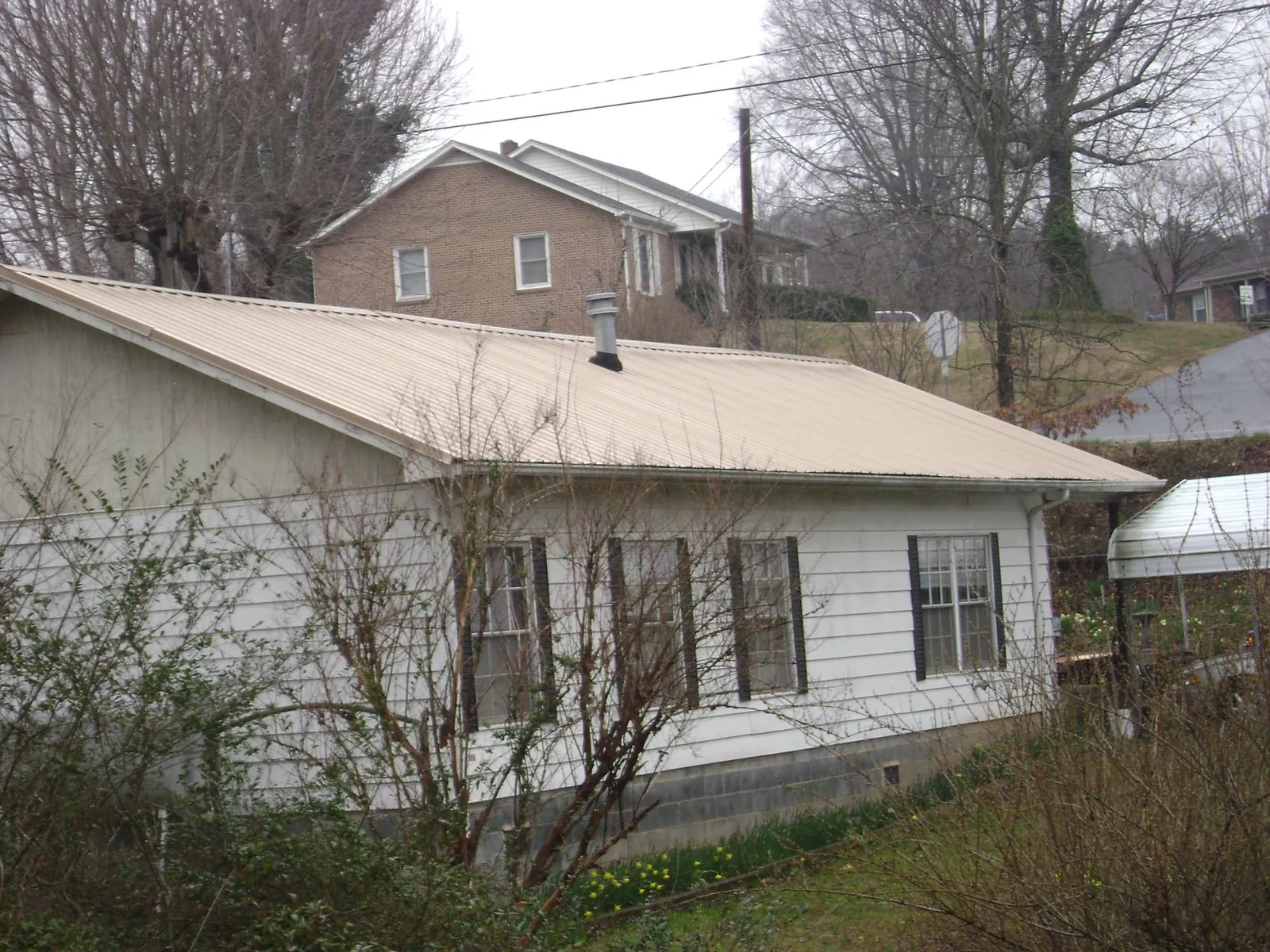 Tan metal roof on a white sided house set into a hillside — Commercial Roofing by Roofing Brothers in Tavernier